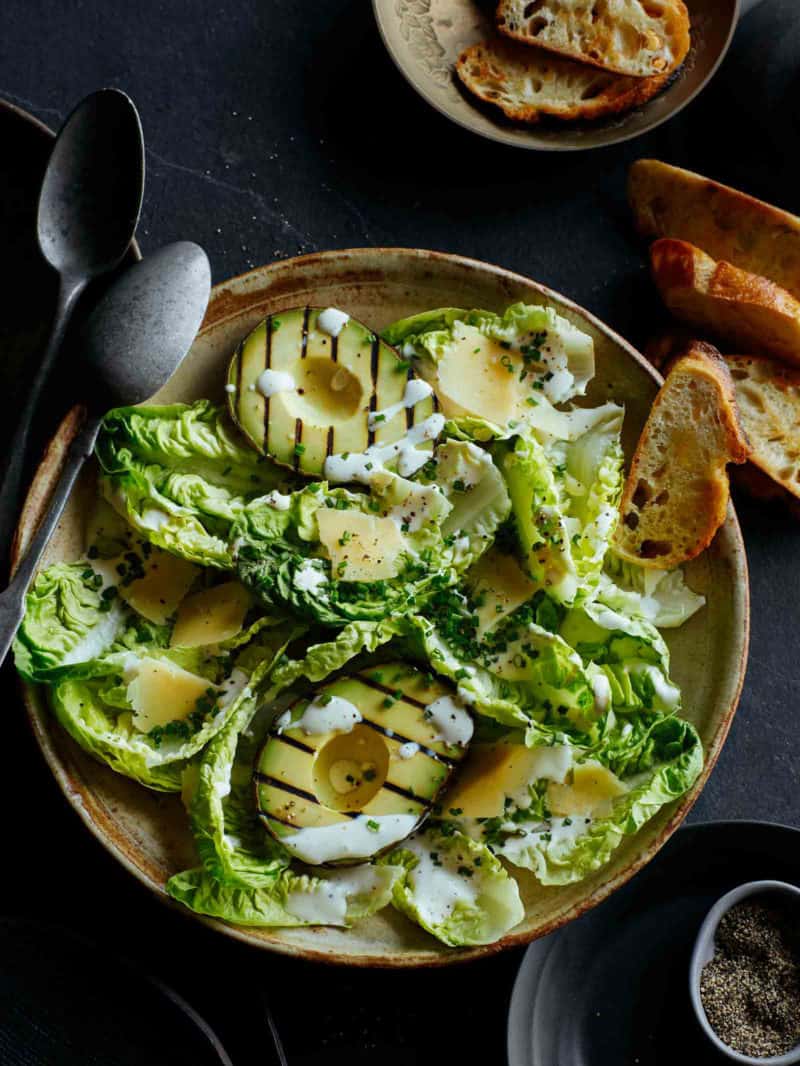 A plate of grilled avocado salad with bread and spoons.