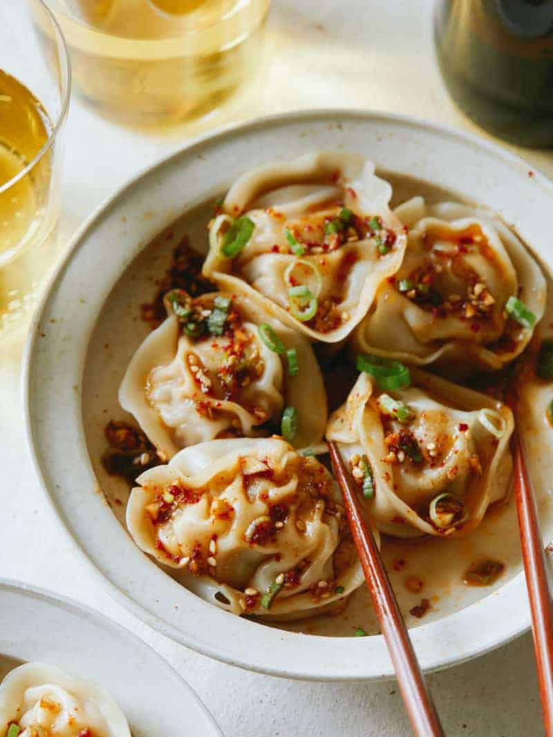 Pork and shrimp dumplings in a bowl with chopsticks and wine on the side. 