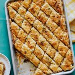 A tray of savory baklava with pieces served on a plate.