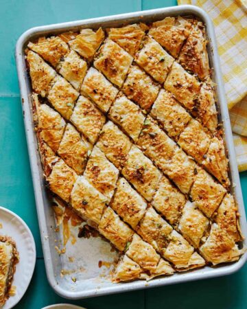 A tray of savory baklava with pieces served on a plate.