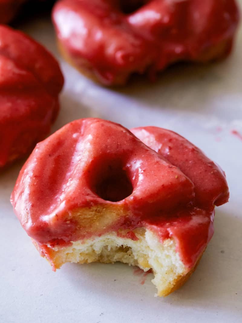 A close up image of one Strawberry Glazed Donut with a bite taken out.