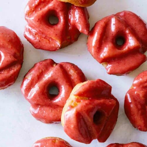 A close up of strawberry glazed old fashioned doughnuts.