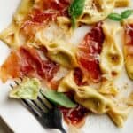 A close up of sweet pea caramelle with prosciutto and a fork.