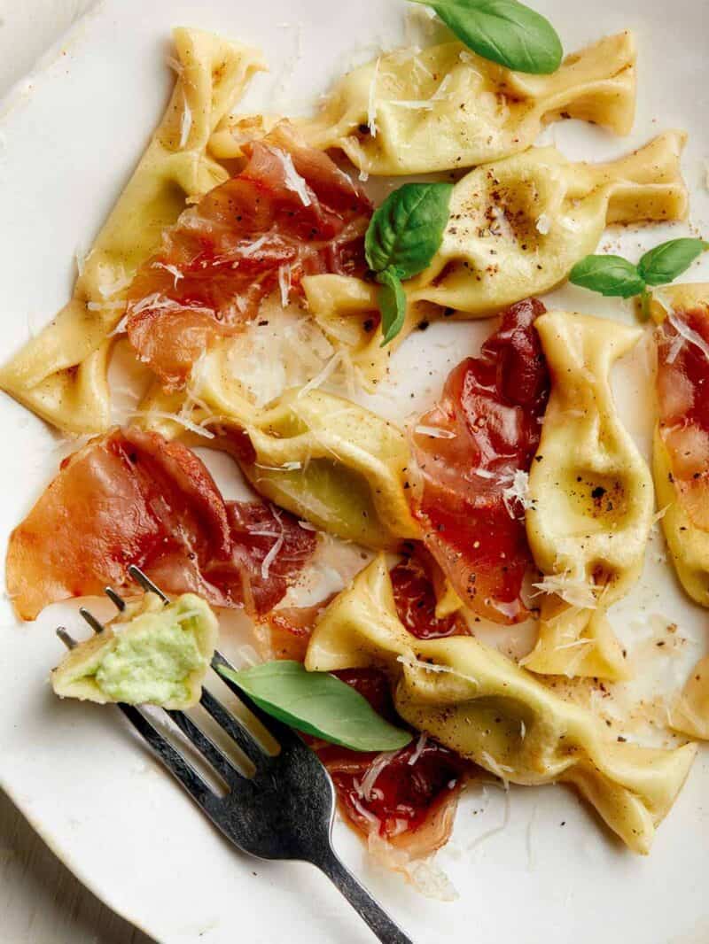 A close up of sweet pea caramelle with prosciutto and a fork.