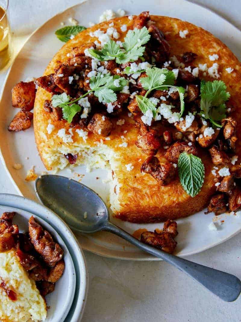 Spiced chicken topped tahchin on a plate served with a spoon.