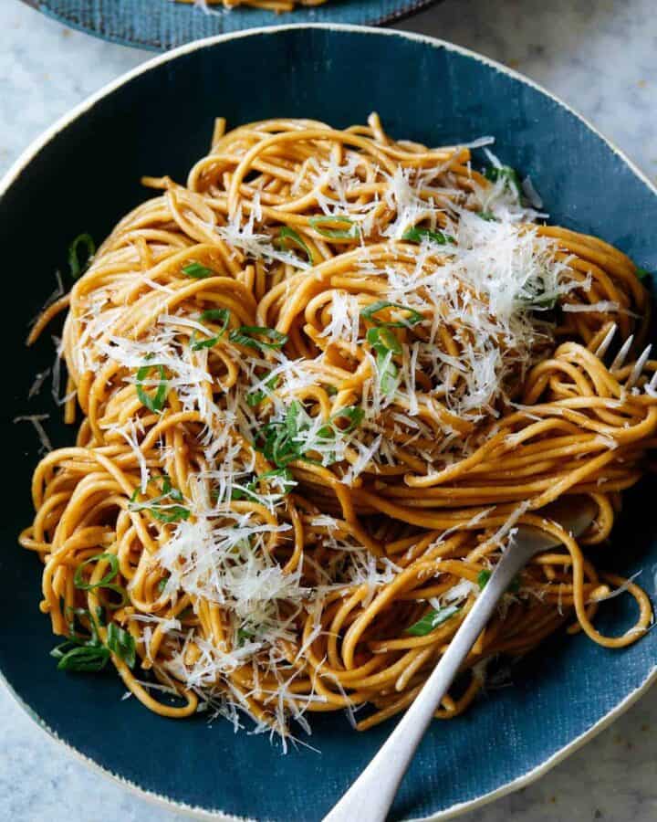 Garlic noodles garnished with cheese on a blue plate with a fork.