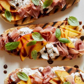 A close up of grilled flatbreads topped with peach, prosciutto, and burrata.