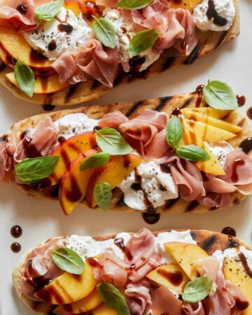 A close up of grilled flatbreads topped with peach, prosciutto, and burrata.