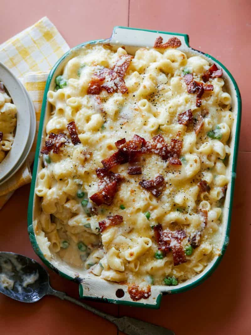A baking pan of creamy baked carbonara mac and cheese with plates and napkins.