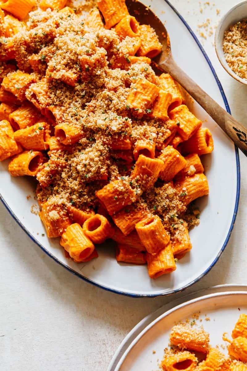 A platter of romesco rigatoni sauce with some served on a plate next to the platter.