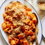Romesco sauce rigatoni topped with breadcrumbs on a platter with a spoon.