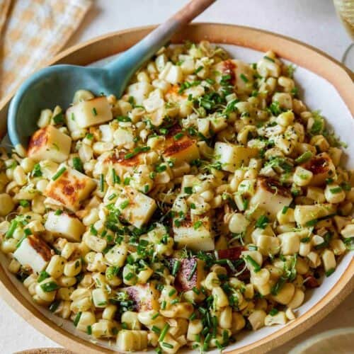 A close up of a bowl of corn salad with a spoon.