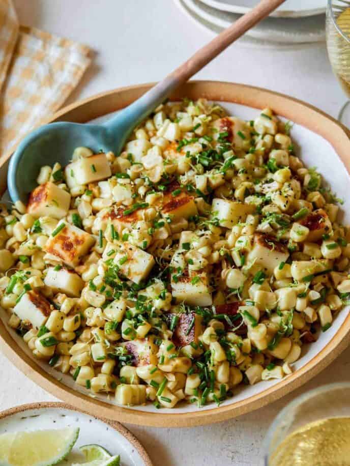 A close up of a bowl of corn salad with a spoon.