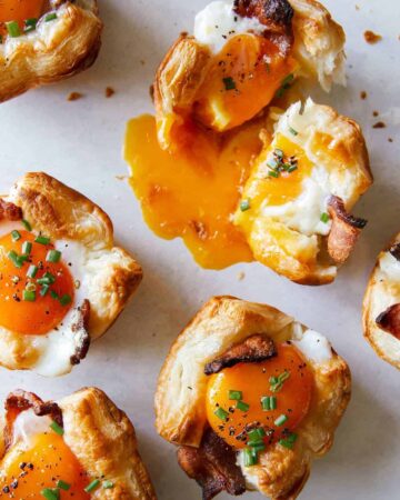 A close up of cheesy flaky breakfast cups with broken yolk.