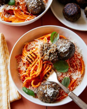 Vegan creamy roasted red pepper spaghetti and meatballs in a bowl with a fork.