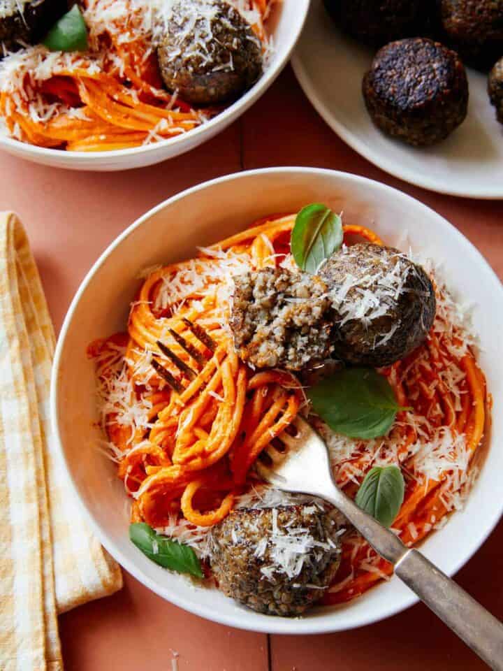 Vegan creamy roasted red pepper spaghetti and meatballs in a bowl with a fork.