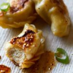 A close up of crispy chicken potstickers with green onions and sauce.