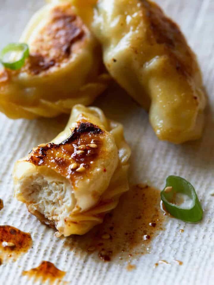 A close up of crispy chicken potstickers with green onions and sauce.