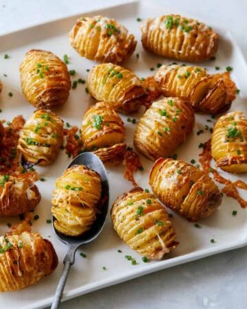 Mini cheesy hasselback potatoes with one on a spoon.