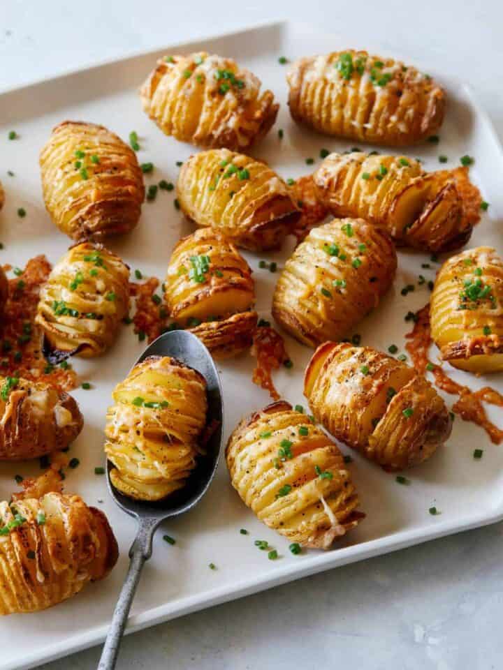 Mini cheesy hasselback potatoes with one on a spoon.