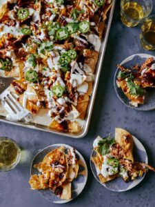 A sheet pan of chipotle chicken nachos with servings on small plates.