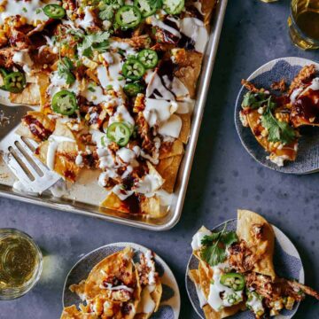 A sheet pan of chipotle chicken nachos with servings on small plates.