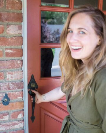 A beautiful blue eyed woman smiling while holding a door handle.