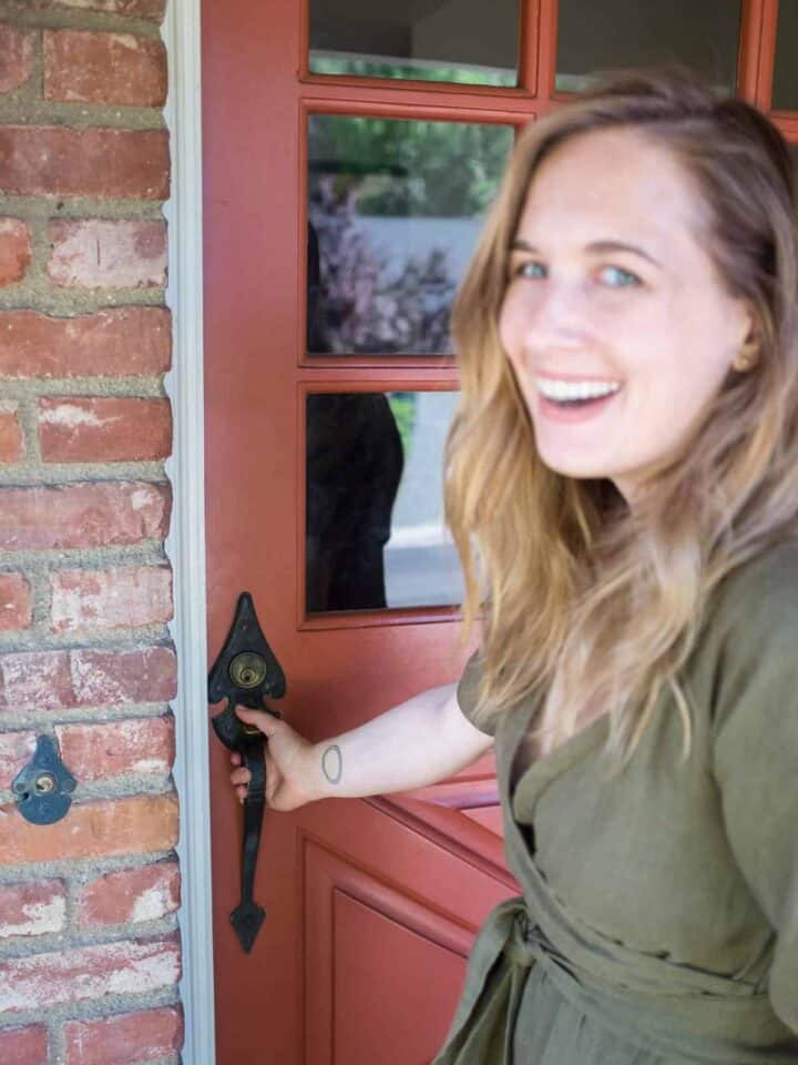 A beautiful blue eyed woman smiling while holding a door handle.