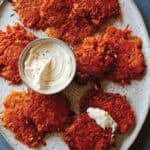 Cheesy sweet potato fritters on a plate with a small bowl of sauce.