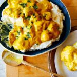 Chicken korma over mashed potatoes with a spoon.