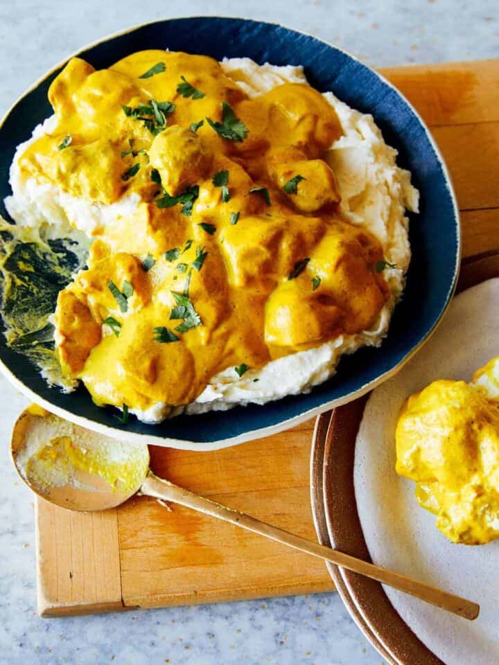 Chicken korma over mashed potatoes with a spoon.