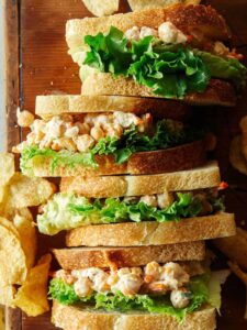 Lined up chickpea salad sandwiches  with potato chips.