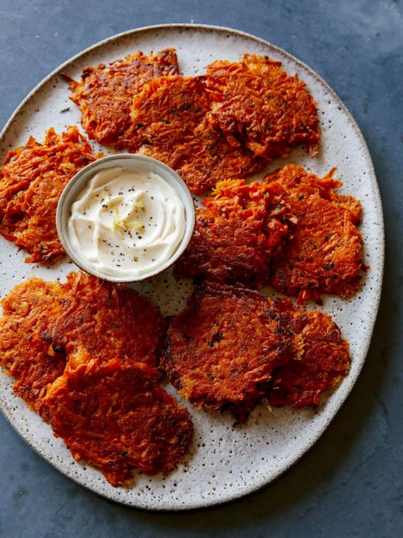Sweet Potato Fritters on a platter served with a ramekin of sour cream. 