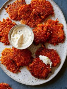 Cheesy sweet potato fritters on a plate with a small bowl of sauce.