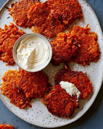 Cheesy sweet potato fritters on a plate with a small bowl of sauce.