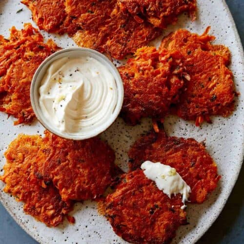 Cheesy sweet potato fritters on a plate with a small bowl of sauce.
