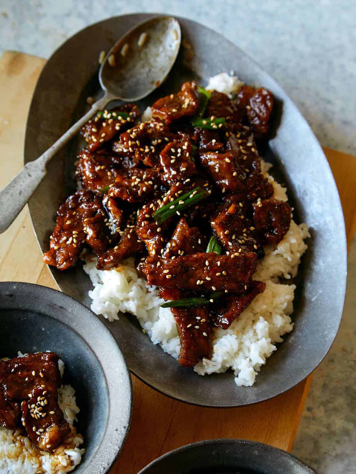 A platter of Mongolian BBQ beef on a bed of rice with sesame seeds and green onions.