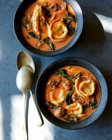 Creamy tortellini with sausage and spinach soup in blue bowls with spoons.