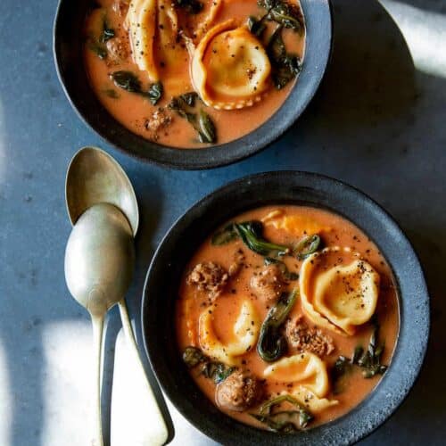 Creamy tortellini with sausage and spinach soup in blue bowls with spoons.