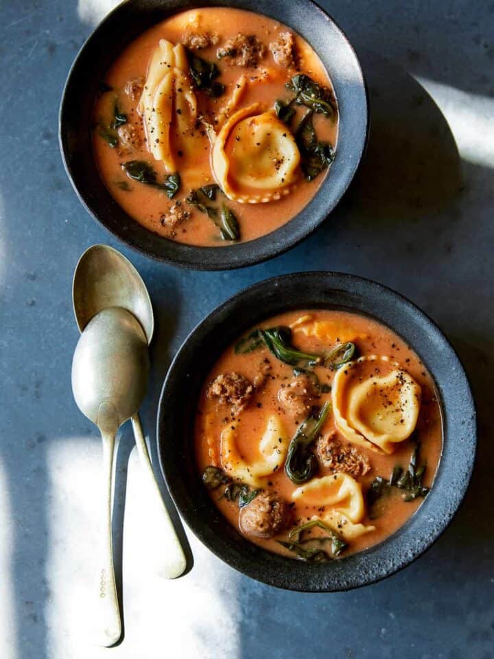 Creamy tortellini with sausage and spinach soup in blue bowls with spoons.
