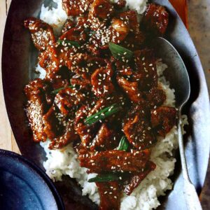 A close up of Mongolian beef on white rice with a spoon.