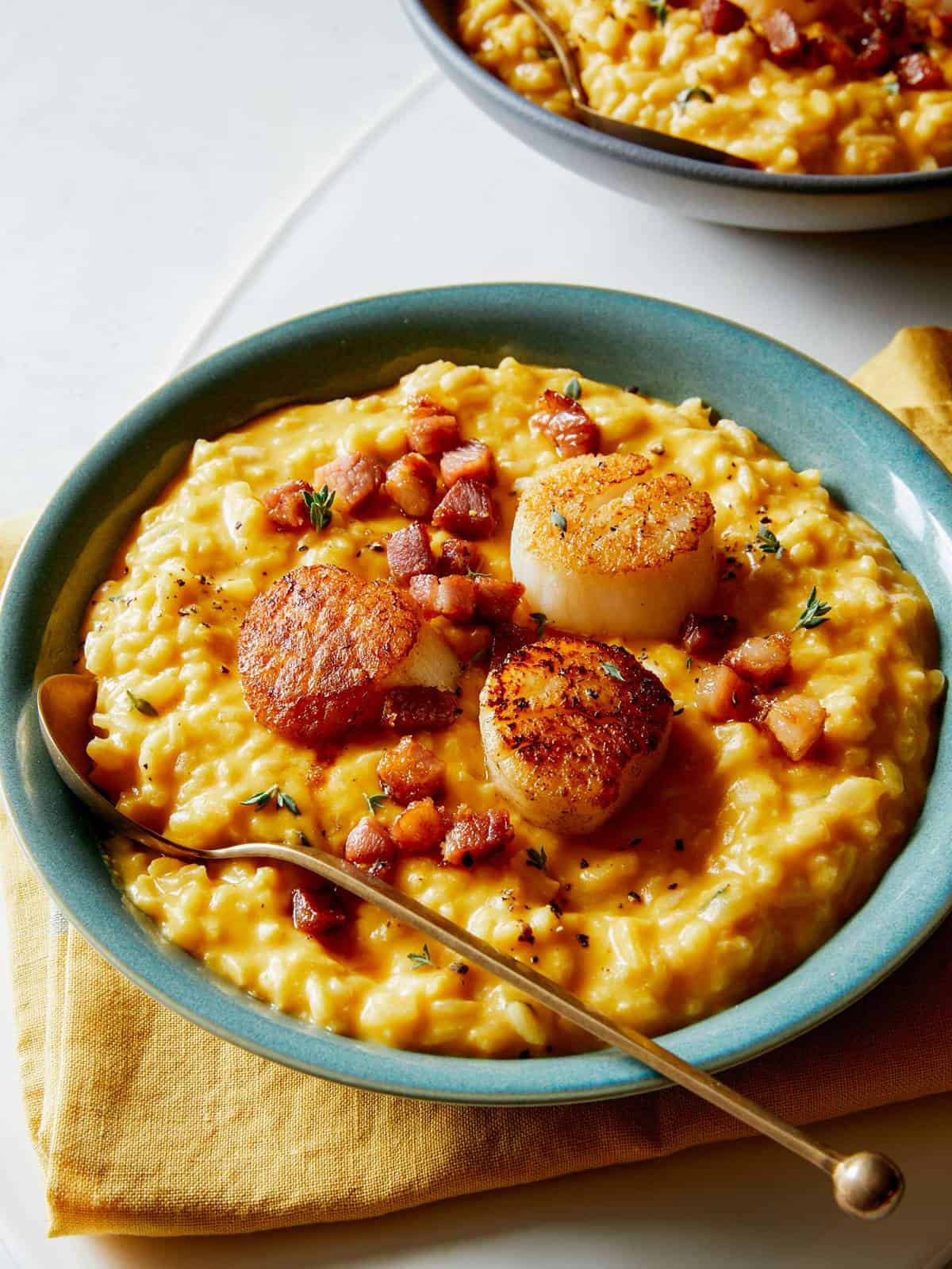 A close up of a bowl of pumpkin risotto with seared scallops and a spoon.