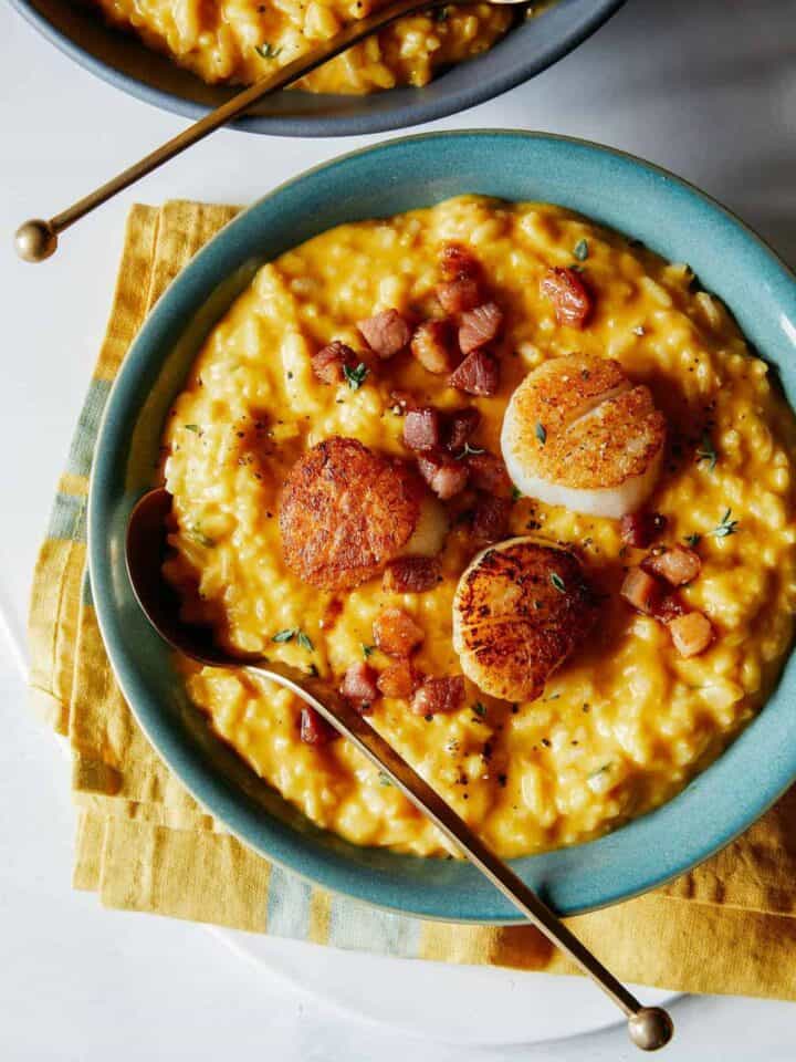 Seared scallops over pumpkin risotto in a blue bowl with a spoon.
