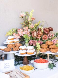 Several cake stands full of doughnuts with a floral arrangement.