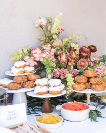 Several cake stands full of doughnuts with a floral arrangement.