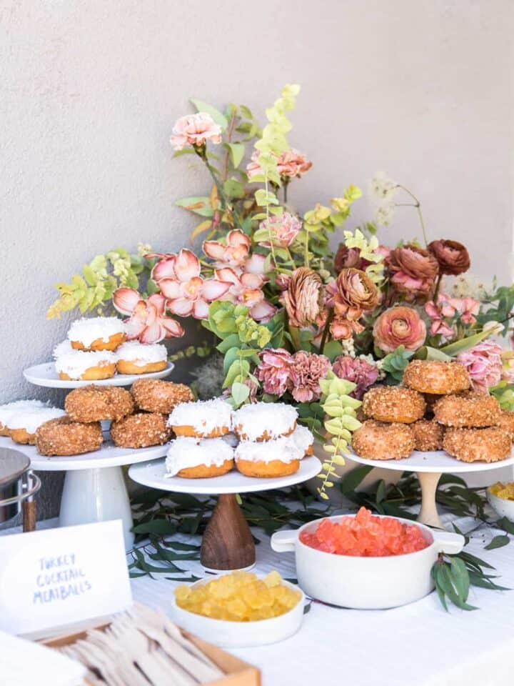 Several cake stands full of doughnuts with a floral arrangement.