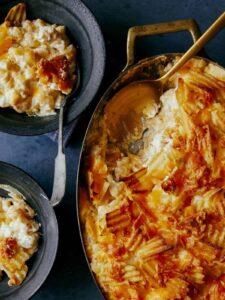 Cheesy potatoes with caramelized onions in a pan with servings and a spoon.