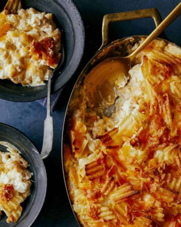 Cheesy potatoes with caramelized onions in a pan with servings and a spoon.