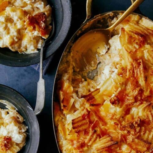 Cheesy potatoes with caramelized onions in a pan with servings and a spoon.