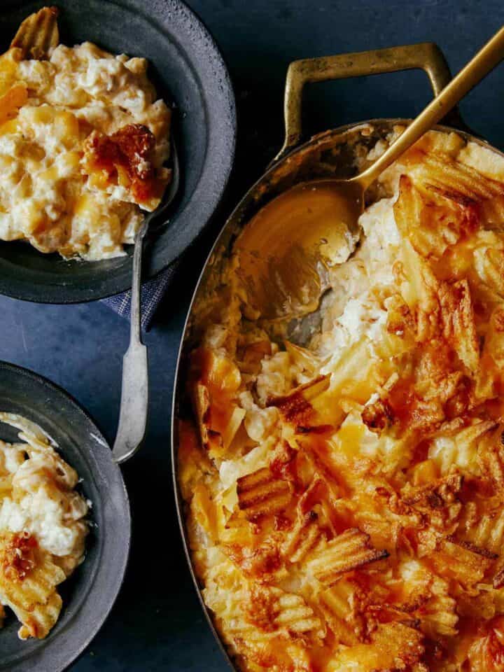 Cheesy potatoes with caramelized onions in a pan with servings and a spoon.